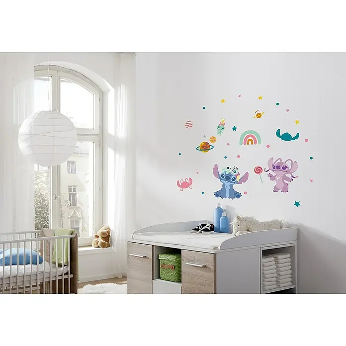 Komar Wandtattoo Stitch World - Bunt, 35 -tlg. - Ein Kinderzimmer mit einem Wickeltisch, der mit Stitch-Wandaufklebern verziert ist, und einem Babybett mit einem blauen Kissen.