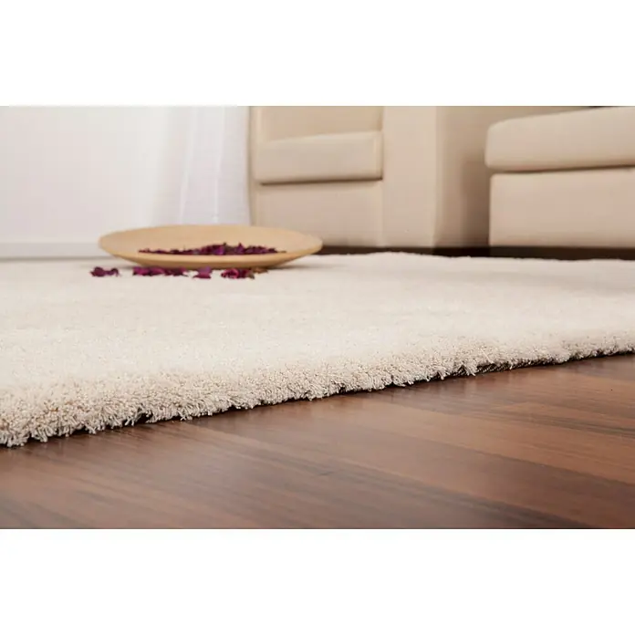 Hochflorteppich Super Soft ShaggyIvory, 230 x 160 cm, 100 % Polyester (Flor) - Nahaufnahme eines beigen Teppichs auf Holzboden mit Schale und Blütenblättern, ideal für ein gemütliches Wohnambiente.