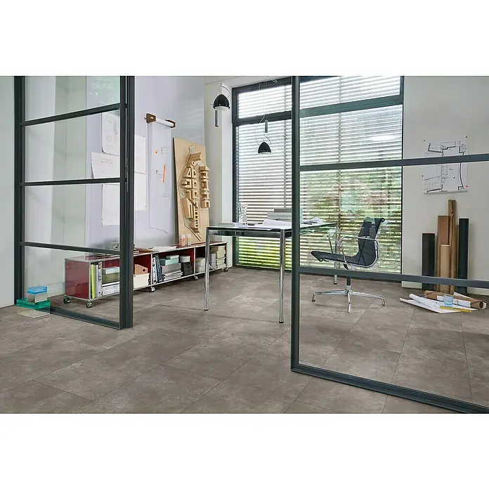 Parador Designboden Modular One - Beton dunkelgrau, Fliese, 853 x 400 x 8 mm - Ein Innenraum mit grauen Fliesen und einer Glaswand, die einen Blick auf einen Schreibtisch und einen Bürostuhl freigibt, schafft eine moderne Arbeitsatmosphäre.