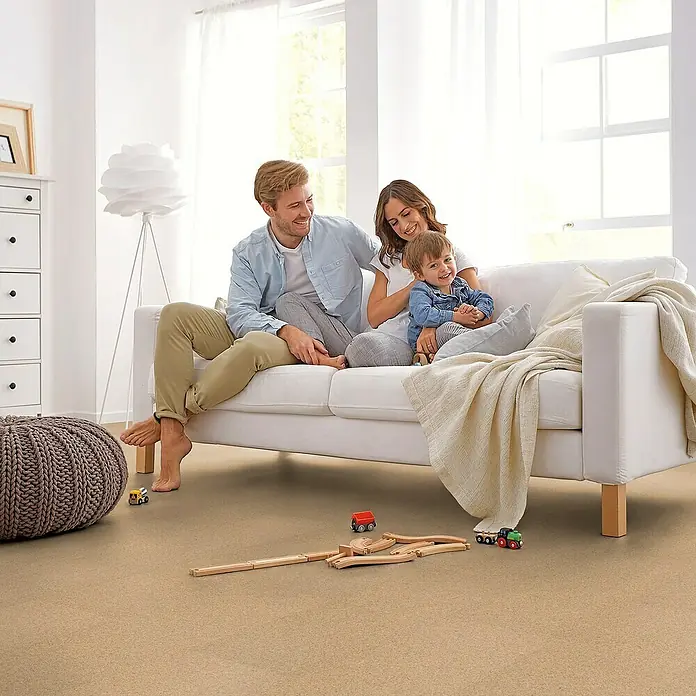 Corklife Korkboden - Sand Creme, 905 x 295 x 10,5 mm - Ein helles Wohnzimmer mit einer Familie auf einem Sofa. Der Fokus liegt auf dem Bodenbelag in Holzoptik, der dem Raum Wärme verleiht.