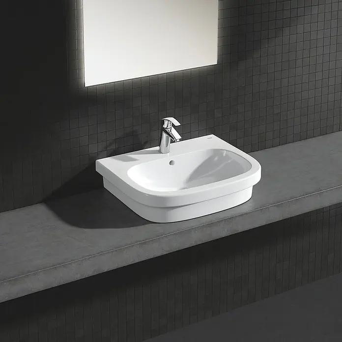 Grohe Eurosmart Waschtischarmatur M-Size - Mit Zugstange, Chrom, Glänzend - Elegantes Waschbecken-Design mit Chromarmatur auf einer grauen Ablagefläche vor dunklen Mosaikfliesen und einem hellen Spiegel.