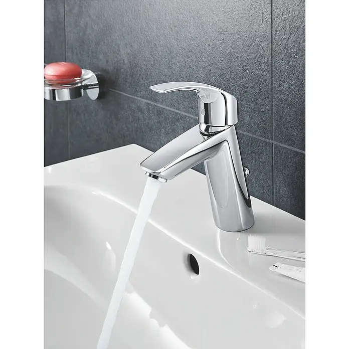 Grohe Eurosmart Waschtischarmatur M-Size - Mit Zugstange, Chrom, Glänzend - Nahaufnahme eines glänzenden Chrom-Wasserhahns, der in ein weißes Waschbecken montiert ist, mit fließendem Wasser.