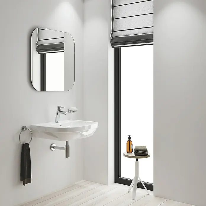 Grohe Concetto Waschtischarmatur M-Size - Ohne Zugstange, Chrom, Glänzend - Ein modernes Badezimmer mit einem weißen Waschbecken, einem abgerundeten Spiegel und einem kleinen Beistelltisch neben einem Fenster mit Rollo.