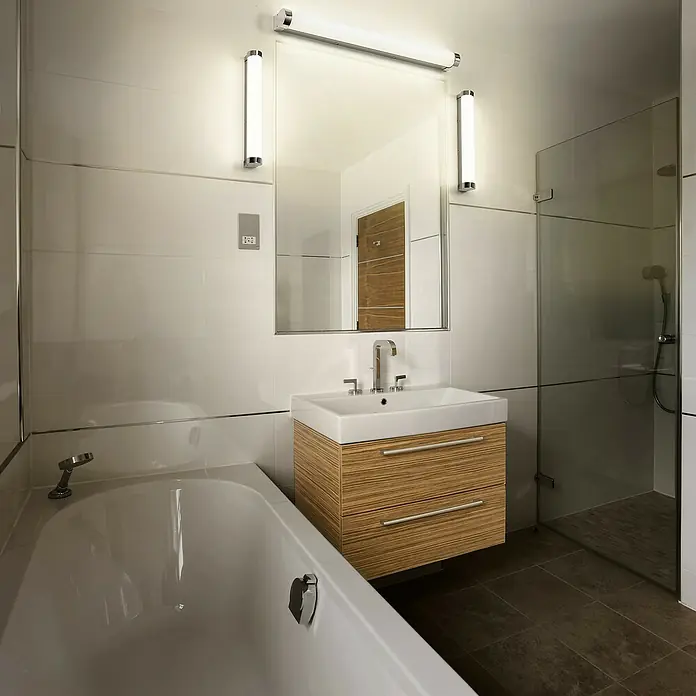 Ledvance Orbis LED-Spiegelleuchte Tube - 9 W, L x B x H: 40 x 7 x 5,4 cm, Chrome, Frostglas, Warmweiß - Ein helles Badezimmer mit einem modernen Waschtisch mit Schubladen, einem Spiegel und einer Badewanne.\n