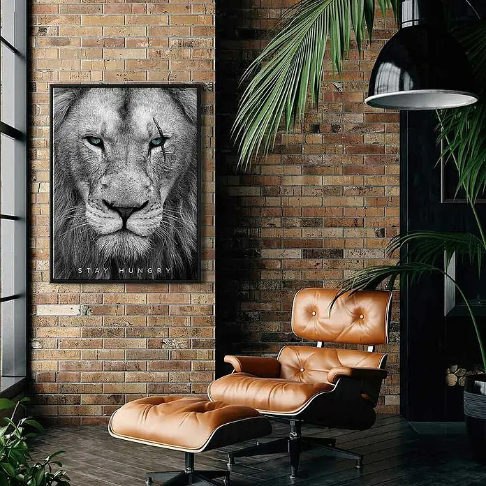 Dotcomcanvas Leinwandbild - Hungry Face, B x H: 60 x 80 cm - Das Bild zeigt ein stilvolles Wohnzimmer mit einem braunen Ledersessel und einem Löwenbild mit der Aufschrift "Stay Hungry" an der Wand.