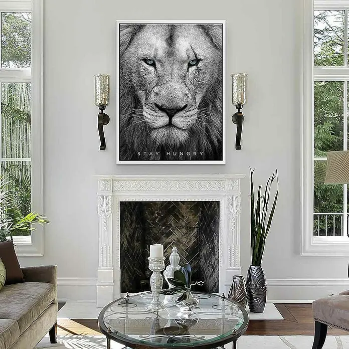 Dotcomcanvas Leinwandbild - Hungry Face, B x H: 60 x 80 cm - Wandbild eines Löwen mit blauen Augen und dem Schriftzug "Stay Hungry", umrahmt von einer modernen Inneneinrichtung.