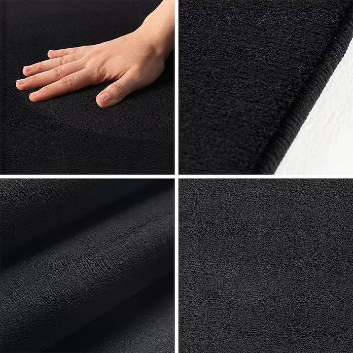 Kurzflorteppich Sky - Schwarz, Durchmesser: 160 cm, 100 % Polyester - Weiche, strukturierte schwarze Stoffmatte, eine Hand berührt die Oberfläche, um ihr Plüschgefühl hervorzuheben.