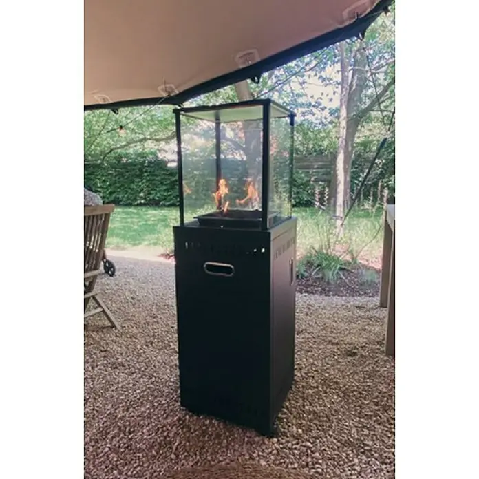Outr Estufa de exterior Ibiza - 9 kW, Altura: 134,5 cm - Foto exterior de un calentador de patio con carcasa de vidrio. El calentador está colocado sobre un camino de grava.
