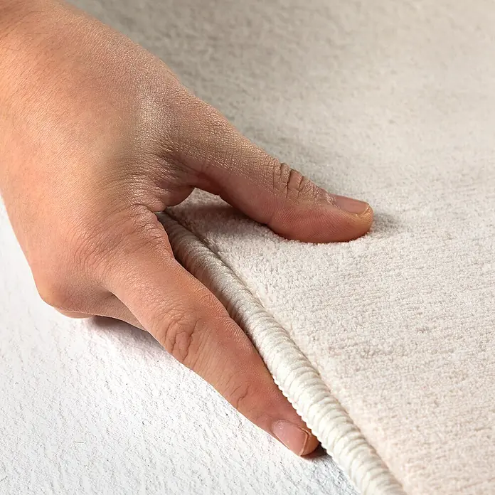 Kurzflorteppich Sky - Creme, Durchmesser: 200 cm, 100 % Polyester - Nahaufnahme einer Hand, die ein luxuriöses, weißes Badematten-Set berührt, das für Komfort und Stil im Badezimmer entwickelt wurde.