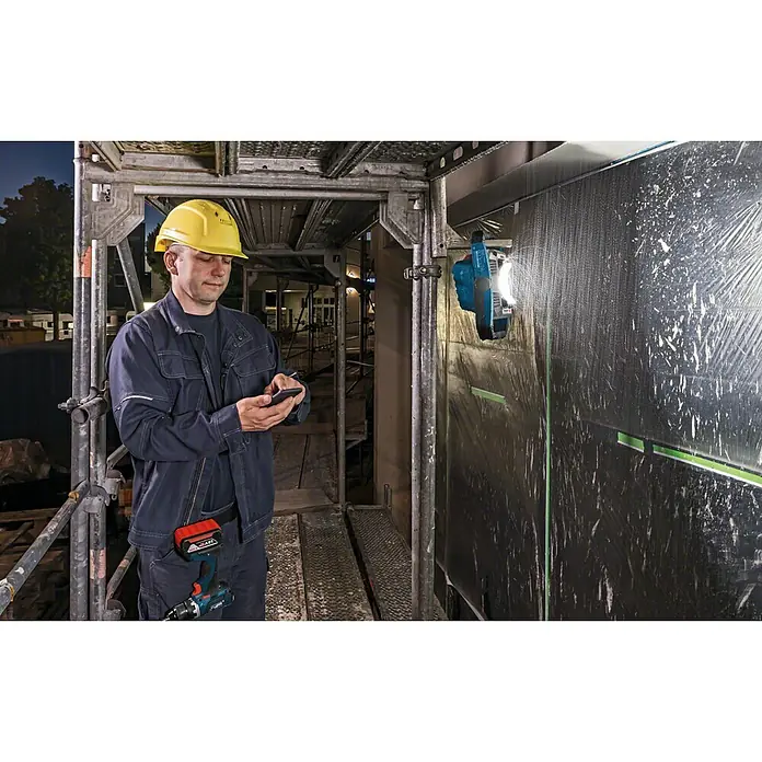 Bosch Professional AMPShare 18V LED-Akkustrahler GLI 18V-1900 - 18 V, Ohne Akku, Lichtstrom: 1.900 lm - Ein Bauarbeiter auf einem Gerüst mit einem Handy in der Hand, neben einer akkubetriebenen Arbeitsleuchte.