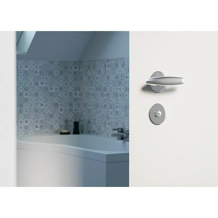 Hoppe Zimmertürgarnitur WC New York - Stärke Tür: 42 mm - 37 mm, Aluminium, Silber, Schlitzkopf/Olive - Türbeschlag in Silber an einer weißen Tür mit Blick in ein Badezimmer. Der Türbeschlag ist modern und schlicht gehalten.