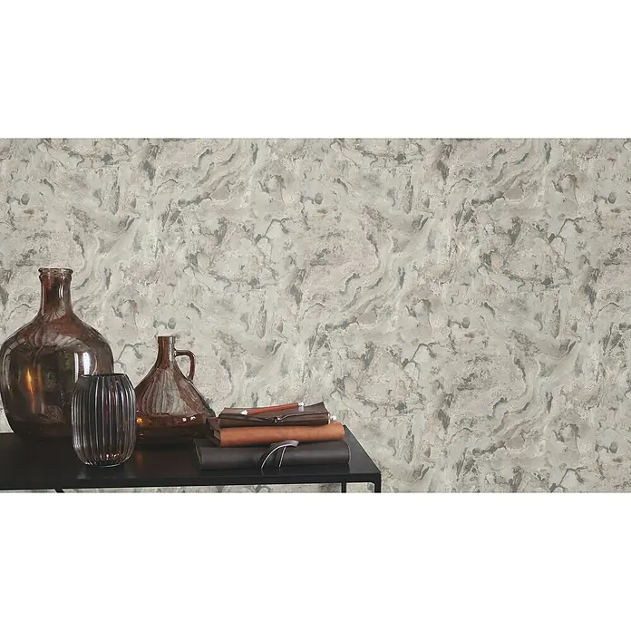 Rasch Symphony Vliestapete Marmor - Mittelgrau, Steinoptik, 10,05 x 0,53 m - Dekorative braune Glasvasen und Notizbücher auf einem schwarzen Tisch vor einer strukturierten Wand.