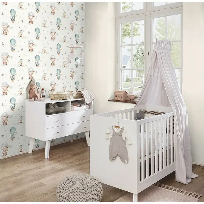 Rasch Kids World Vliestapete Ballon - Helltürkis, Tieroptik, 10,05 x 0,53 m - Ein Kinderzimmer mit einem weißen Kinderbett, einer Kommode und einer Tapete mit Heißluftballons.