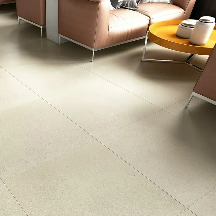 Art-Tec by Palazzo Feinsteinzeugfliese60 x 60 cm, Offwhite, Matt - Nahaufnahme eines Raumes mit beigen Bodenfliesen, einem orangefarbenen Tisch und Sofas. Perfekt für modernes Innendesign.