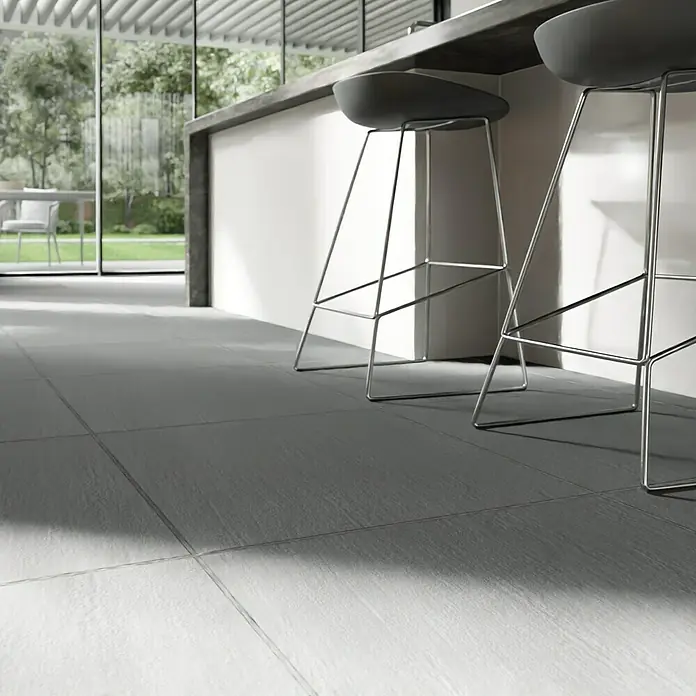 Terrassenfliese Slate Grey60 x 60 x 2 cm, Grau, Matt - Diese Aufnahme zeigt einen stilvollen Innenraum mit modernen Barhockern vor einer Kücheninsel und grauen Bodenfliesen.