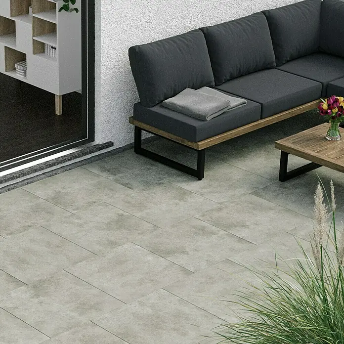 Cersanit Terrassenfliese Metropolis - 59,3 x 59,3 x 2 cm, Light Grey, Matt - Bild eines Außenbereichs mit grauen Terrassenplatten, einer Couch und einem Tisch. Perfekt für entspannte Stunden im Freien.