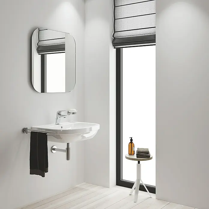 Grohe Eurostyle Waschtischarmatur S-Size - Chrom, Glänzend, Kaltwasserstart - Eine moderne Badezimmeransicht mit einem eleganten Waschbecken, einem stilvollen Spiegel und einem Hocker neben dem Fenster.