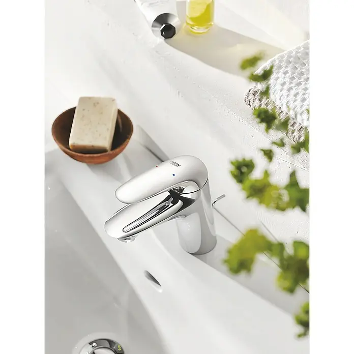 Grohe Eurostyle Solid Waschtischarmatur S-Size - Chrom, Glänzend, Mit Zugstange - Nahaufnahme einer Grohe-Armatur in einem Badezimmerwaschbecken, umgeben von Seife und einer Tube Lotion.