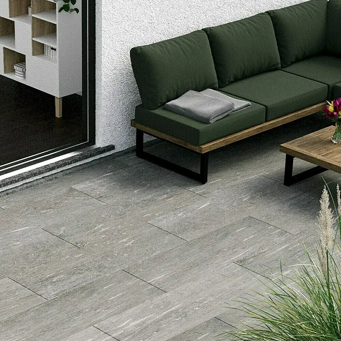 Esterno 20 T by Palazzo Terrassenfliese Davos - 40 x 120 x 2 cm, Greige, Matt - Bild einer modernen Terrasse mit grauen Fliesen, einer grünen Lounge-Garnitur und einem Holztisch im Freien. Die grauen Fliesen schaffen eine stilvolle Atmosphäre.