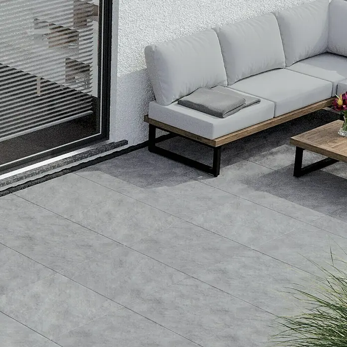 Terrassenfliese Atakama - 59,3 x 59,3 x 2 cm, Hellgrau, Matt - Ein elegantes Außensofa mit hellgrauen Kissen und einem Holztisch auf einer modern gestalteten Terrasse mit grauen Fliesen.