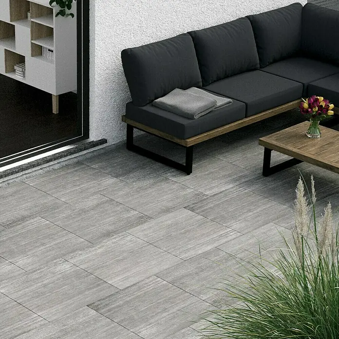 Terrassenfliese Garden Grey Struktur - 59,7 x 59,7 x 2 cm, Grau, Matt - Ein stilvoller Außenbereich mit grauen Terrassenplatten, einem modernen Sofa und einem passenden Couchtisch, ideal für entspannte Stunden im Freien.