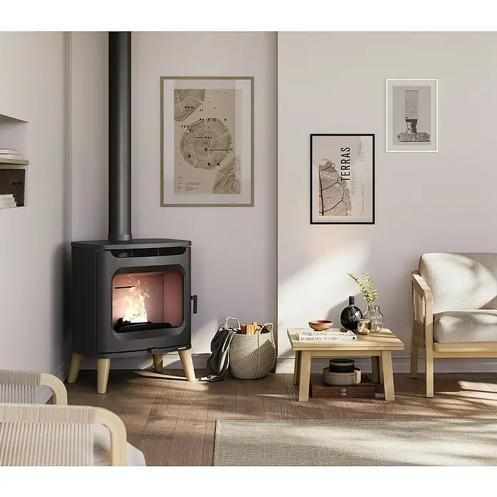 FreePoint Estufa de leña Flos Wood - 7 kW, Volumen de calefacción: 196 m³, Negro - La imagen muestra una estufa de leña moderna con un fuego crepitante, rodeada de muebles y decoraciones elegantes en un espacio habitable acogedor.