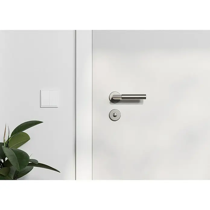 Hoppe Zimmertürgarnitur WC Lecce - Stärke Tür: 42 mm - 37 mm, Aluminium, Schlitzkopf/Olive - Nahaufnahme einer weißen Tür mit einem modernen silbernen Türgriff und einem Schlüsselloch, neben einem Lichtschalter an einer weißen Wand.