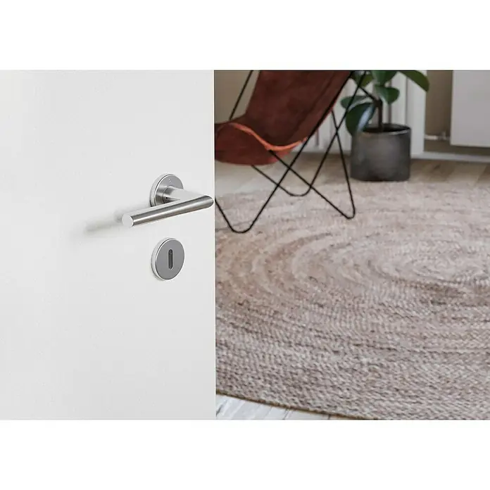 Hoppe WC-Drückergarnitur Stockholm - Stärke Tür: 37 mm - 42 mm, Edelstahl, Buntbart - Nahaufnahme einer Tür mit silberfarbenem Griff und Schlüsselloch, im Hintergrund ein Teppich, ein Sessel und eine Zimmerpflanze.