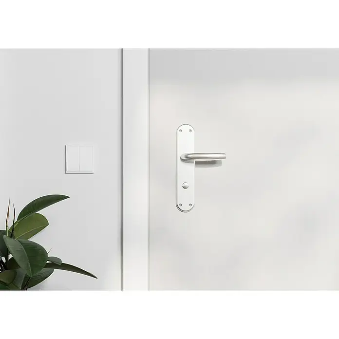 Hoppe WC-Drückergarnitur WC Tokyo - Schlitzkopf/Olive, Aluminium, Langschild - Nahaufnahme einer weißen Tür mit einem stilvollen, silbernen Türgriff und einem Lichtschalter an der Wand.
