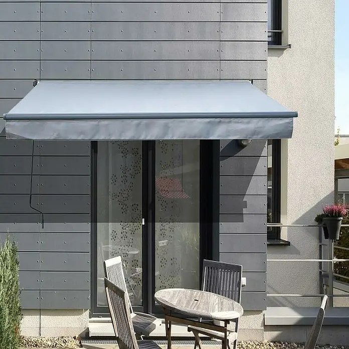 Toldo de brazos extensibles Basic - Gris, Ancho: 2,5 m, Caída: 2 m - Un toldo gris protege una puerta de patio del sol, con una mesa y sillas en frente.