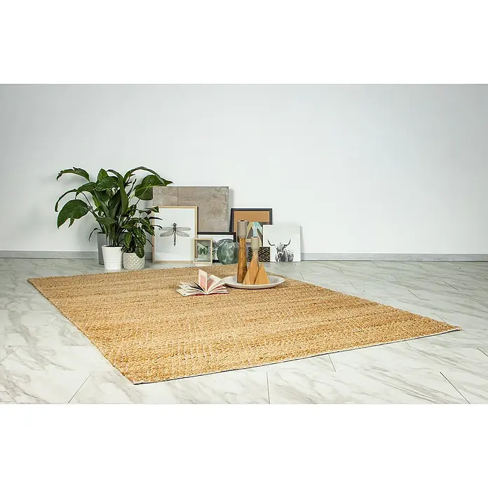Juteteppich Nature 501 - Naturbraun, 230 x 160 cm, 100 % Jute - Nahaufnahme eines beigen Teppichs mit Dekoration wie Pflanzen, Bilderrahmen und Holzobjekten auf einem stilvollen Boden.