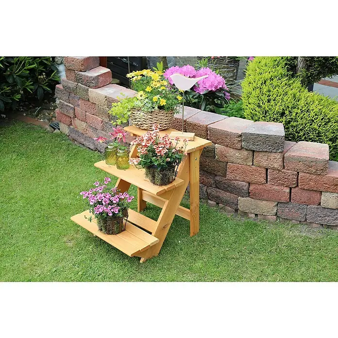 Promadino Blumentreppe - 60 x 50 x 56 cm, Kiefer, Braun - Ein dreistufiges Holzregal im Garten, dekoriert mit Blumen und Pflanzen. Das Regal steht vor einer Mauer aus Ziegelsteinen.