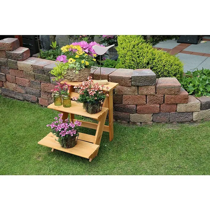 Promadino Blumentreppe - 60 x 50 x 56 cm, Kiefer, Braun - Dreistufige Holzleiter mit bunten Blumenarrangements und dekorativen Vasen vor einer Ziegelmauer.