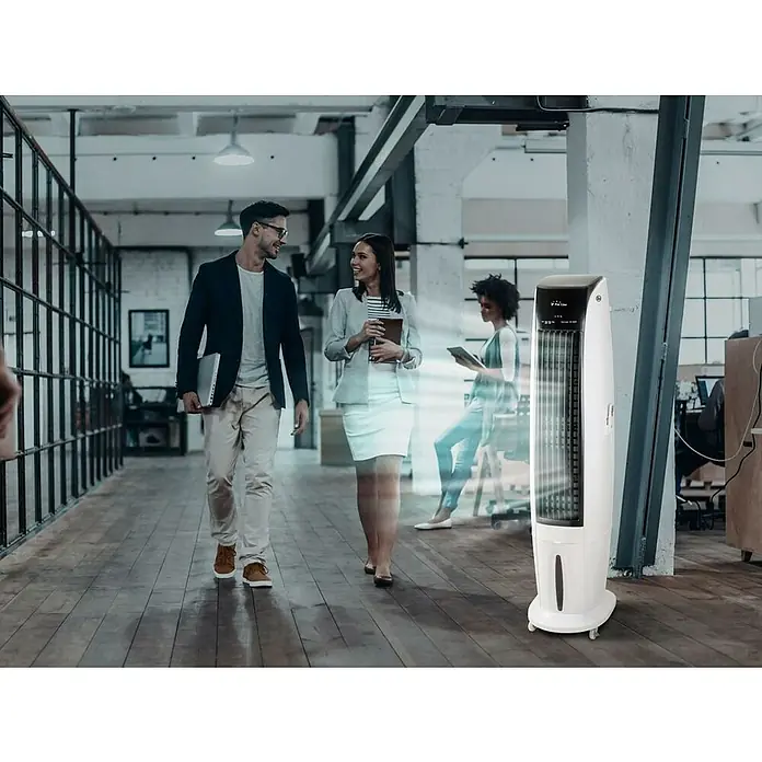 Purline Rafy Climatizador evaporativo 170 - Blanco, Altura: 170 cm, Potencia frigorífica: 350 W, Tamaño de la estancia: 55 m² - Un ventilador de torre blanco y elegante se encuentra en un entorno de oficina, ofreciendo una brisa fresca. Colegas sonrientes charlan al fondo.