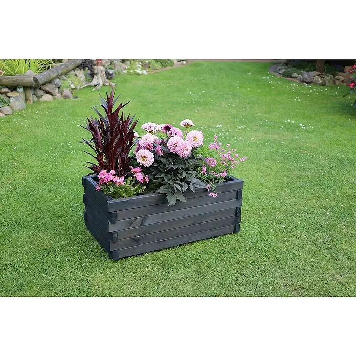 Promadino Pflanzkasten Lucca - Außenmaß (L x B x H): 69 x 39 x 29,5 cm, Holz, Anthrazit - Holzpflanzgefäß mit farbenfrohen Blumen auf saftig grünem Rasen. Das Pflanzgefäß ist grau und mit Holzlatten gefertigt, bepflanzt mit rosa und lila Blumen.