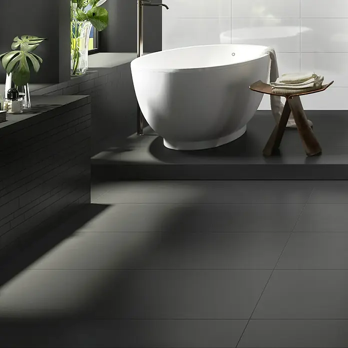 Ambiente by Palazzo Feinsteinzeugfliese - 30 x 60 cm, Schwarz, Matt - Das Bild zeigt ein modernes Badezimmer mit einer freistehenden Badewanne, dunklen Fliesen und minimalistischem Design.
