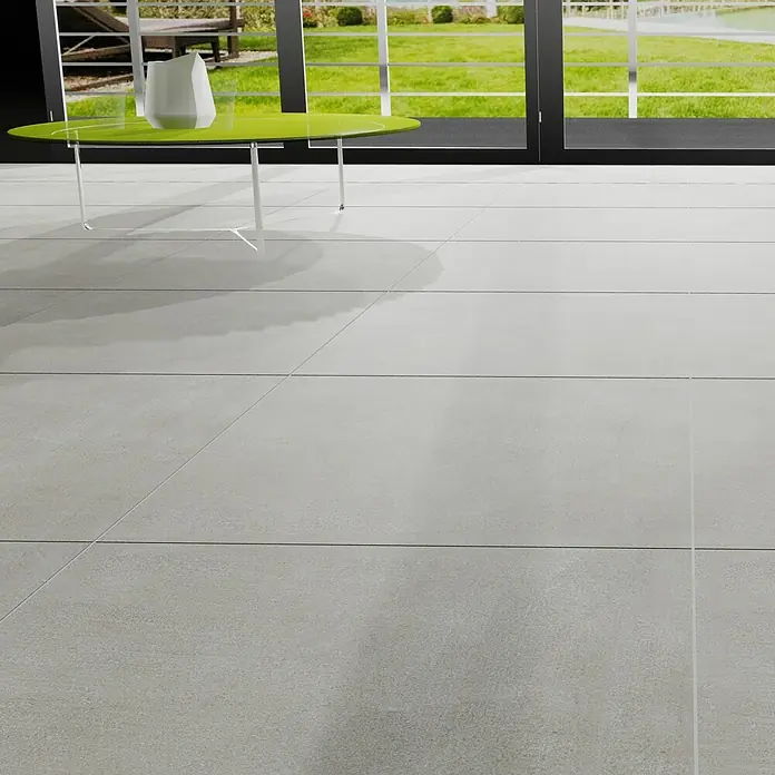 Marazzi Feinsteinzeugfliese Boston - 60 x 60 cm, Grau, Matt - Helle Bodenfliesen in einem modernen Raum mit einem grünen Tisch und einer weißen Vase. Die Fliesen sind großformatig und haben eine matte Oberfläche.