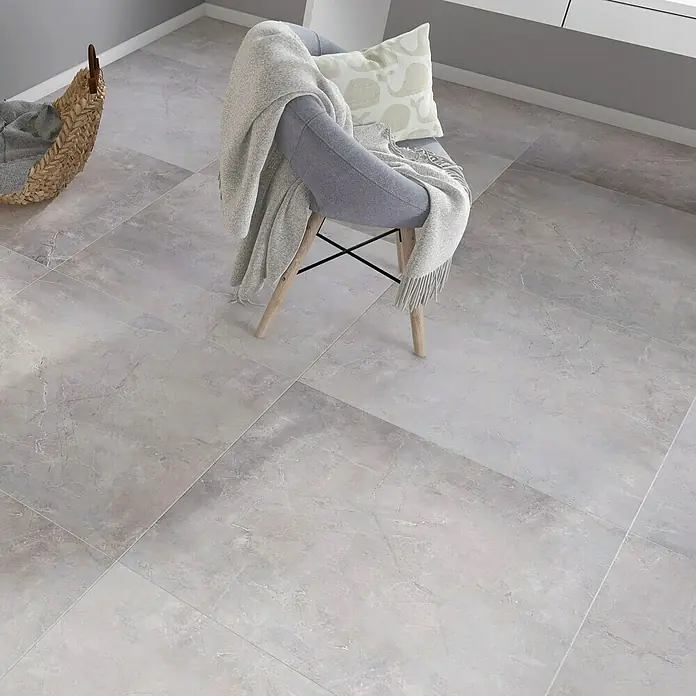 Feinsteinzeugfliese Premium Marble - 80 x 80 cm, Grau, Glänzend - Ein grauer Fliesenboden erzeugt eine ruhige Atmosphäre, ergänzt durch einen Stuhl mit Decke und Kissen für zusätzlichen Komfort.
