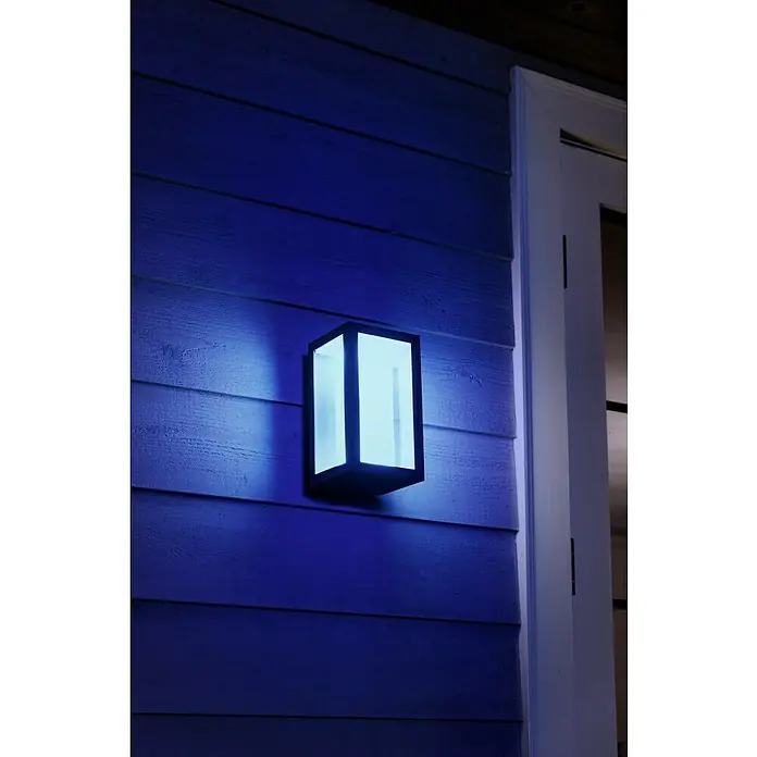 Philips Hue LED-Außenwandleuchte Impress - 8 W, 14,1 x 12 x 24 cm, Schwarz, IP44 - Nahaufnahme einer modernen, rechteckigen Wandleuchte mit blauem Licht an einer Wand neben einer Tür.