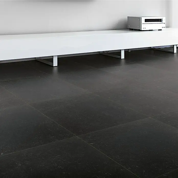 Feinsteinzeugfliese Lanzarote - 60,4 x 60,4 cm, Schwarz, Matt - Produktansicht eines modernen, niedrigen weißen Sideboards mit einem silbernen Gerät darauf, platziert auf einem dunklen Fliesenboden.