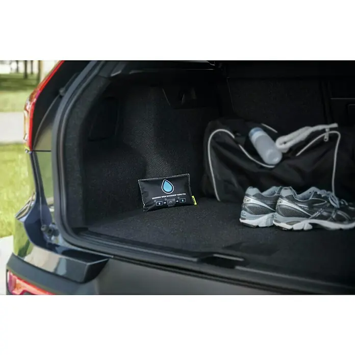 UHU Luftentfeuchter Auto - 300 g - Ein wiederaufladbarer Auto-Luftentfeuchter, der Feuchtigkeit absorbiert und Gerüche beseitigt, liegt im Kofferraum neben einer Sporttasche und Turnschuhen.