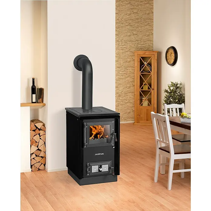 Justus Küchenherd Rustico-50 2.0 - 7 kW, Raumheizvermögen: 144 m³, Schwarz - Ein schwarzer Justus Kaminofen mit brennendem Feuer im Wohnzimmer, daneben Holzscheite und ein Holztisch mit Stühlen.