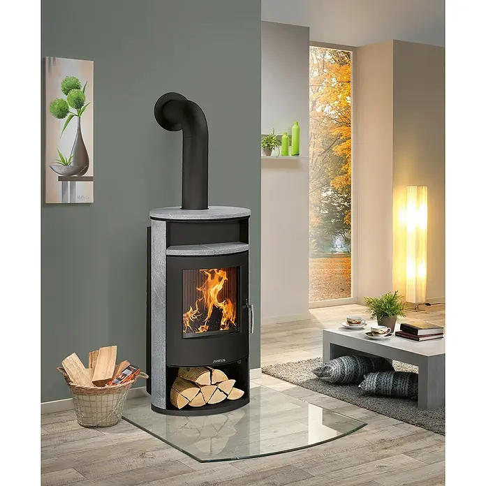 Justus Kaminofen Island Aqua - 10 kW, Raumheizvermögen: 200 m³, Material Verkleidung: Speckstein, Schwarz - Kaminofen mit Holzscheiten im Wohnzimmer. Der Ofen spendet Wärme und sorgt für eine gemütliche Atmosphäre.