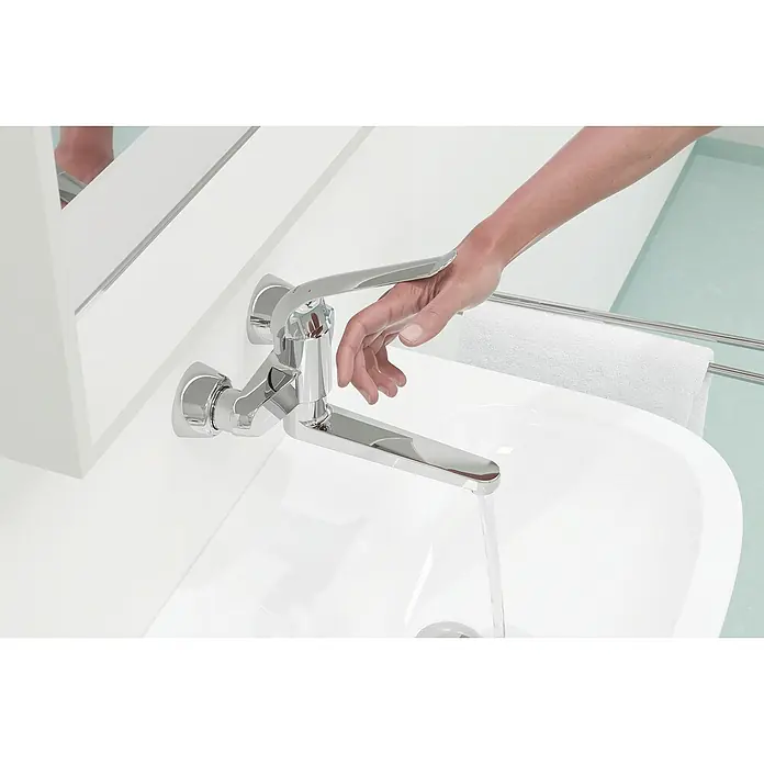 Grohe Euroeco Special Waschtischarmatur - Wandmontage, Chrom, Glänzend, Ausladung Armatur: 257 mm - Nahaufnahme einer modernen Chromarmatur über einem weißen Waschbecken, Wasser läuft, eine Hand reguliert den Wasserhahn.