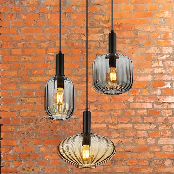 Globo Pendelleuchte Valletta - 60 W, Ø x H: 55 x 150 cm, Amber, Schwarz matt - Drei moderne Hängelampen mit geriffeltem Glasschirm und Edison-Glühbirnen vor einer Backsteinmauer.