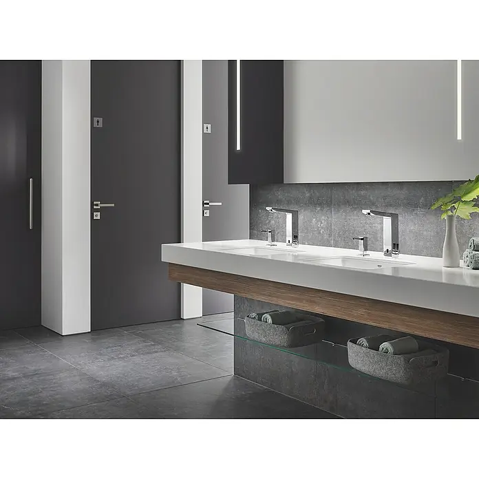 Grohe Eurocube Waschtischarmatur mit Temperaturregulierung, netzbetrieben - Infrarot-Elektronik, Chrom - Ein modernes Badezimmer mit zwei Waschbecken, stilvollen Armaturen und praktischen Ablagekörben für Handtücher.