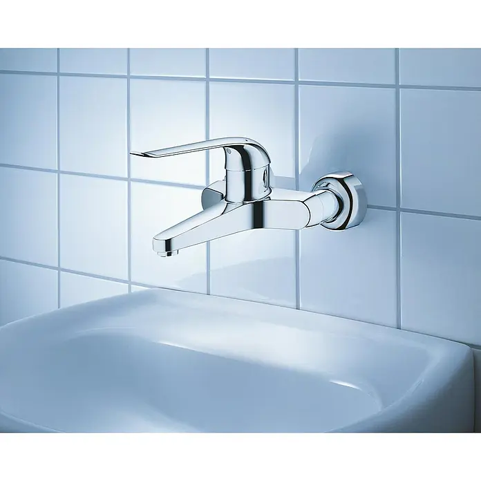 Grohe Euroeco Special Waschtischarmatur - Wandmontage, Chrom, Glänzend, Ausladung Armatur: 204 mm, Mit Einhandbedienhebel - Nahaufnahme eines glänzenden Chrom-Wasserhahns, der an einer mit quadratischen Fliesen versehenen Wand über einem weißen Waschbecken montiert ist.