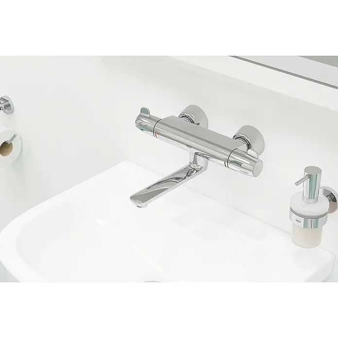 Grohe Grohtherm Special Waschtischarmatur - Chrom - Nahaufnahme einer modernen, verchromten Wandarmatur mit einer Seifenspender- und Toilettenpapierhalterung in einem minimalistischen Badezimmer.