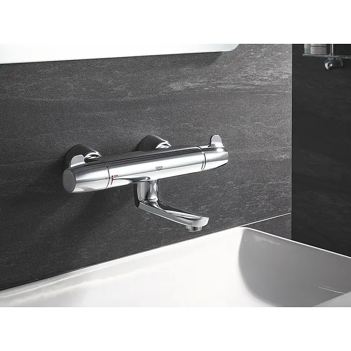 Grohe Grohtherm Special Waschtischarmatur - Chrom - Nahaufnahme eines glänzenden Grohe Thermostat-Wasserhahns an einer dunklen Wand mit einem weißen Waschbecken im Vordergrund.