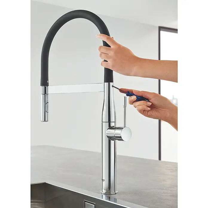 Grohe Essence Spültischarmatur - Chrom, Glänzend - Nahaufnahme einer Person, die mit einem Schraubendreher an einem glänzenden Chrom-Küchenarmatur mit schwarzem, flexiblem Auslauf arbeitet.